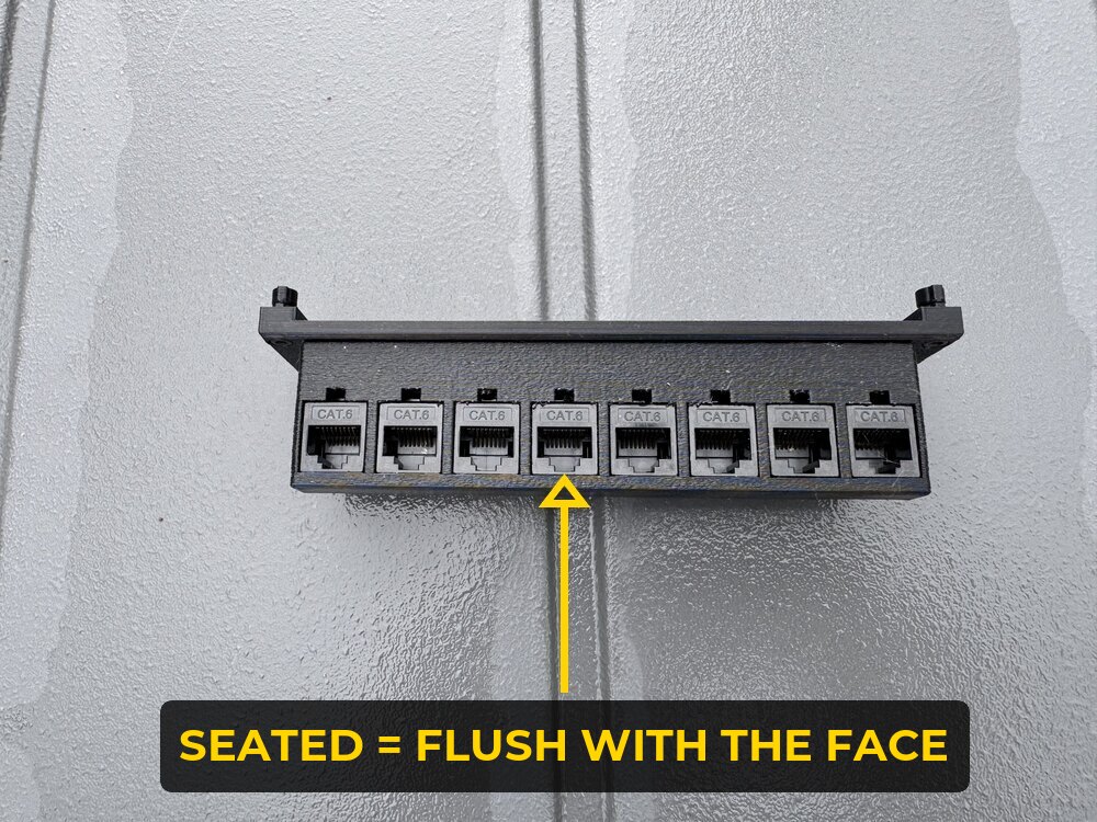 Black 8-port keystone patch panel with eight Cat6 couplers snapped in, labelled to show a seated keystone sits flush with the panel face