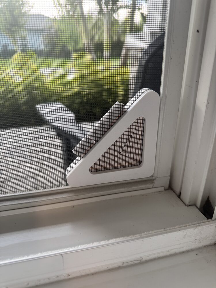 Screen Pass-Thru installed in the lower corner of a window screen, viewed from inside